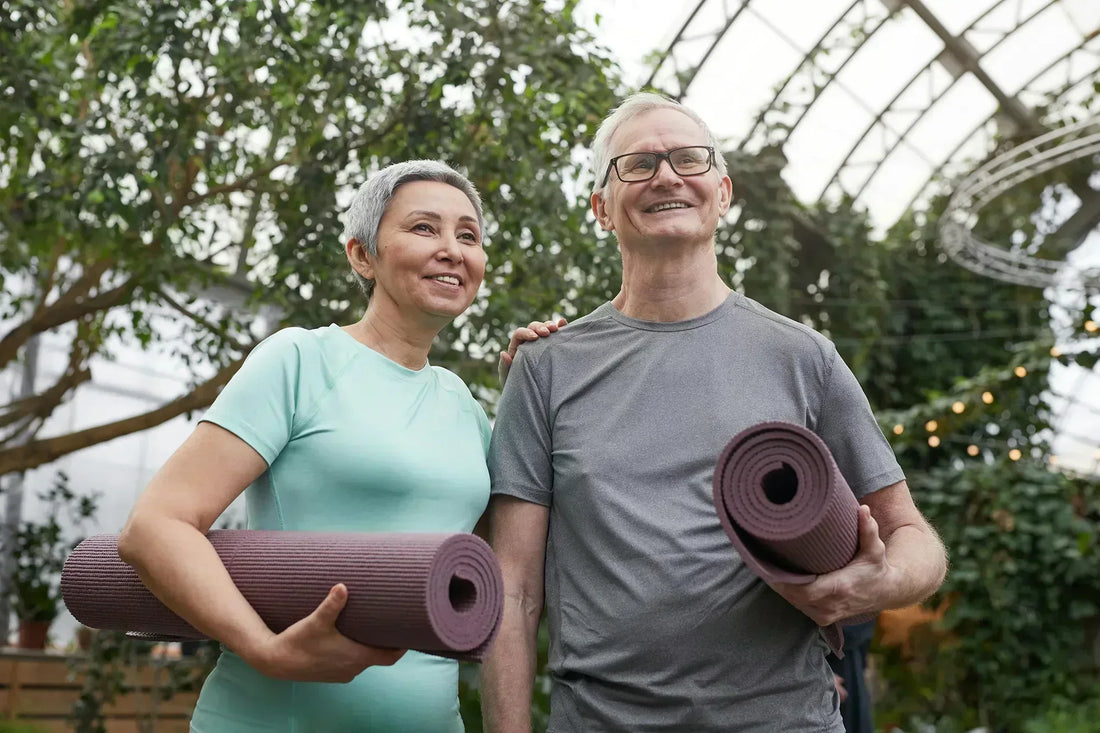 Happy senior couple holding yoga mats in a lush greenhouse setting