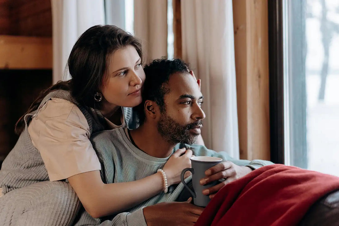 A multiethnic couple enjoys a cozy moment indoors, sitting by a window with a warm embrace