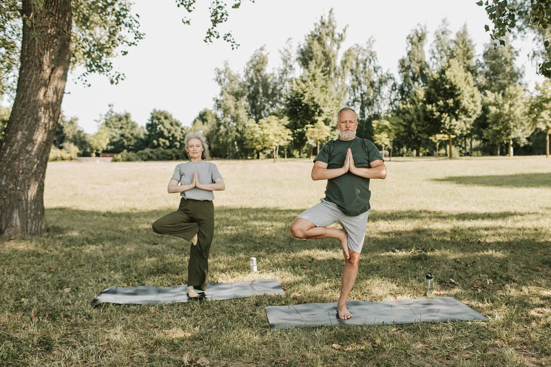 An elderly couple doing yoga in a serene park setting, promoting a healthy lifestyle.