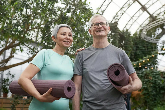 Happy senior couple holding yoga mats in a lush greenhouse setting