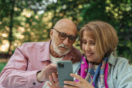 Happy senior couple using smartphone in a park, enjoying sunny outdoors 