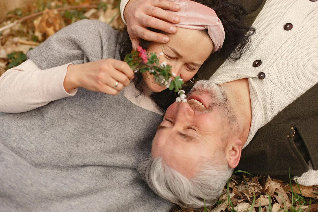 Senior couple lying on grass, smiling with affection, in a warm autumn setting,reflecting intimacy in the context of post-prostate surgery ED.